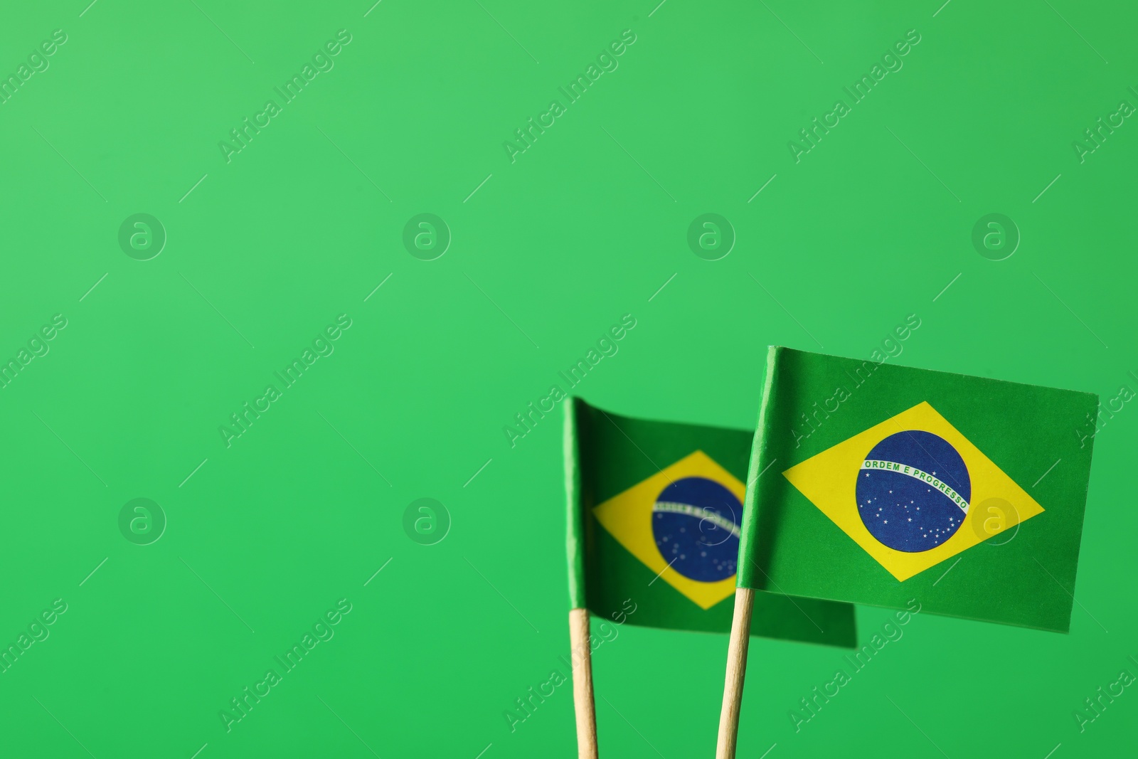 Photo of Small paper flags of Brazil on green background, space for text