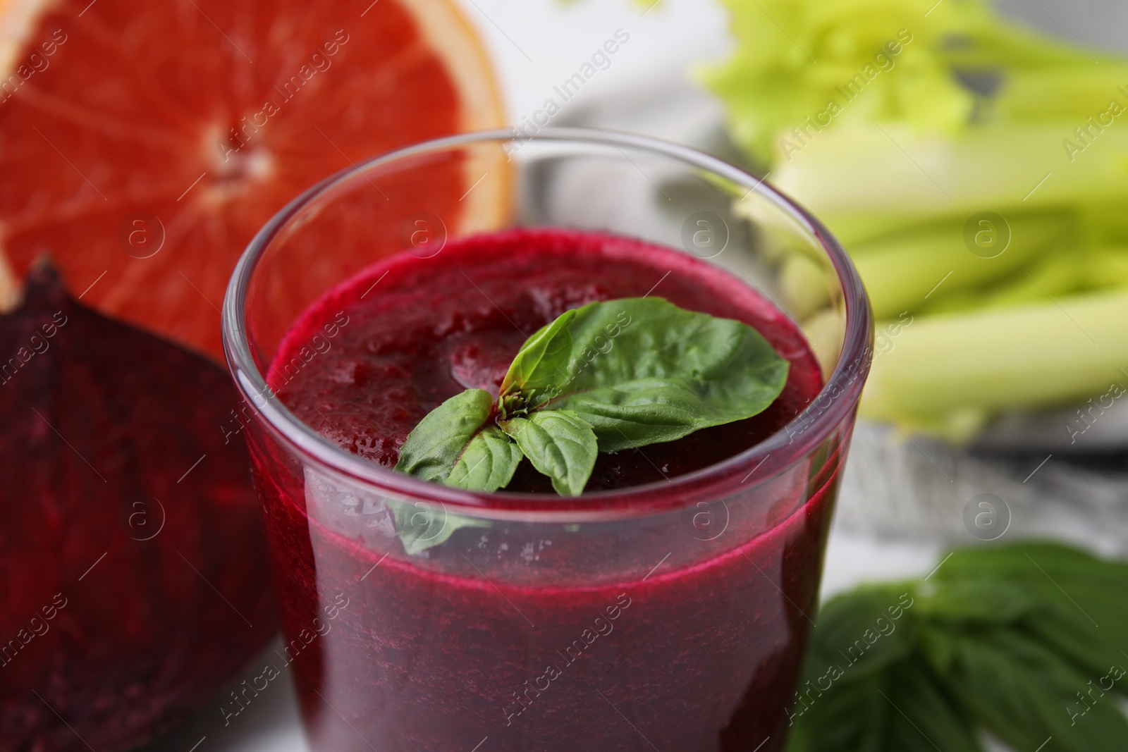 Photo of Tasty beetroot smoothie with basil in glass, fresh vegetables and grapefruit on table, closeup. Vegan drink