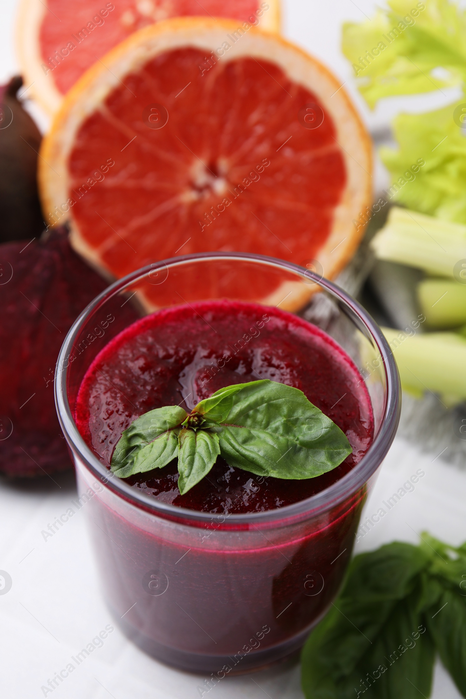 Photo of Tasty beetroot smoothie with basil in glass, fresh vegetables and grapefruits on light table, closeup. Vegan drink