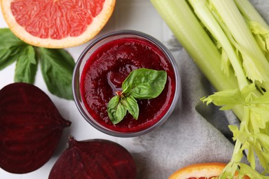 Photo of Tasty beetroot smoothie with basil in glass, fresh vegetables and grapefruit on table, flat lay. Vegan drink