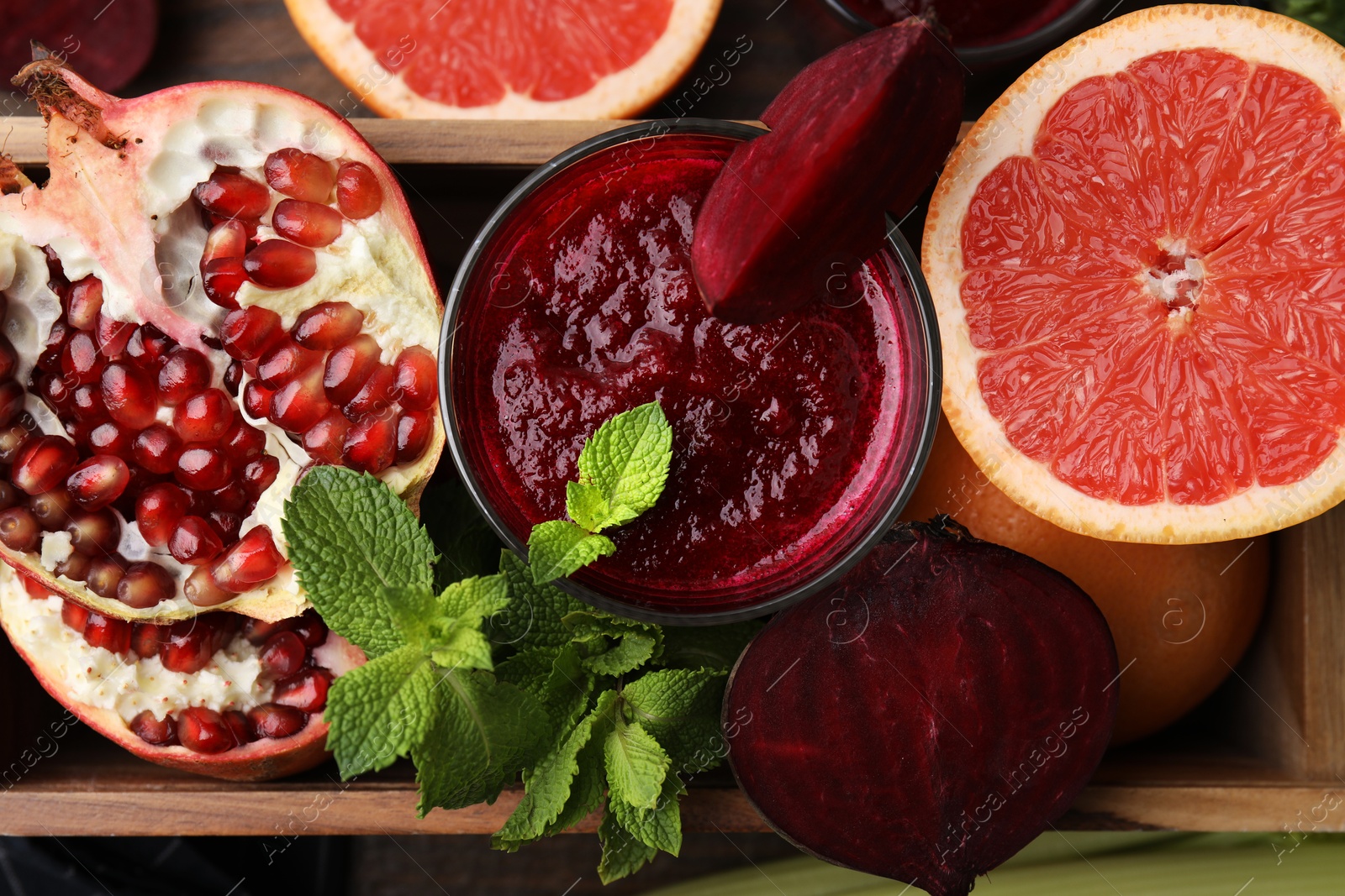 Photo of Glass of tasty beetroot smoothie, fresh vegetables, fruits and mint in wooden box on table, top view. Vegan drink