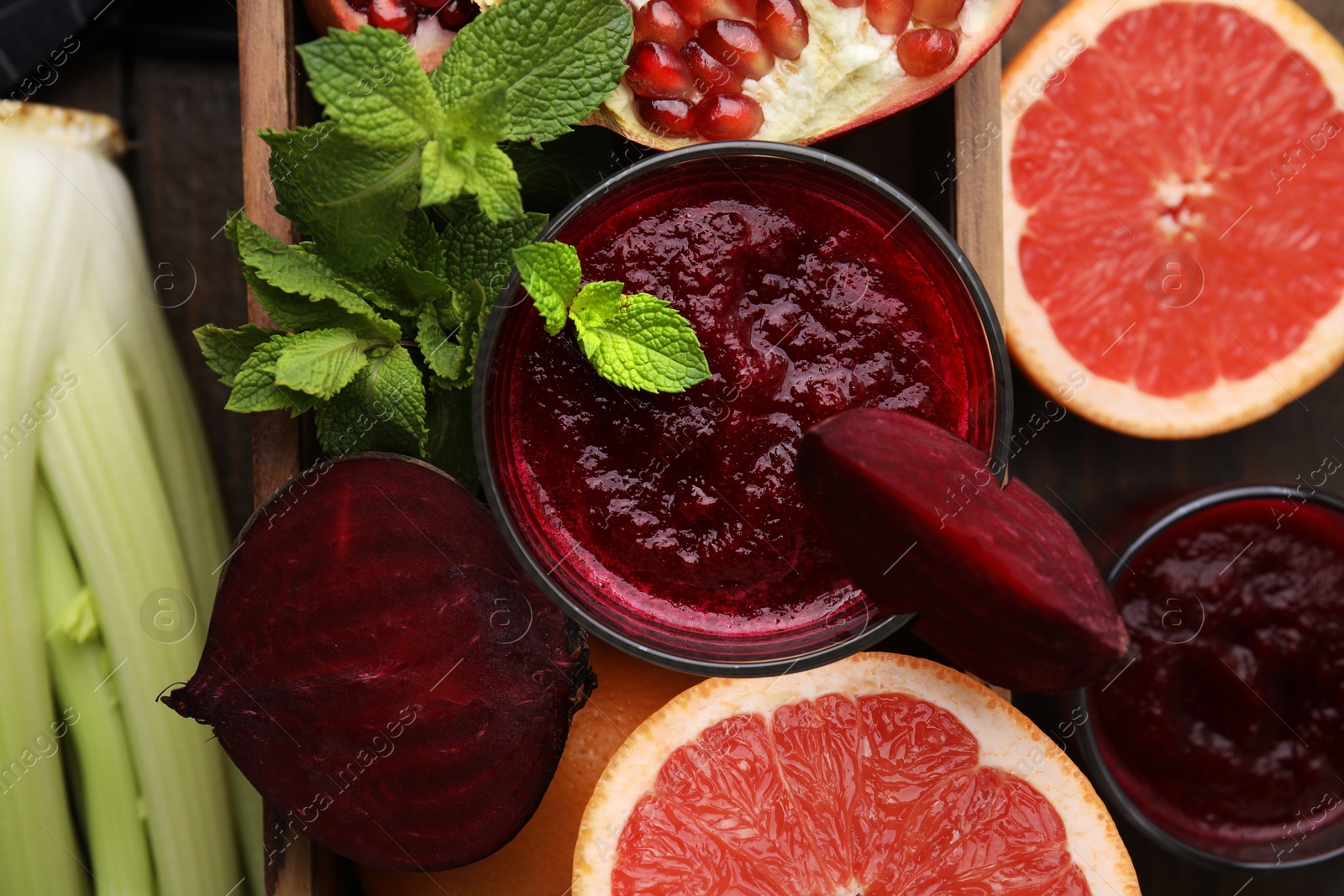 Photo of Glass of tasty beetroot smoothie, fresh vegetables, fruits and mint in wooden box on table, top view. Vegan drink