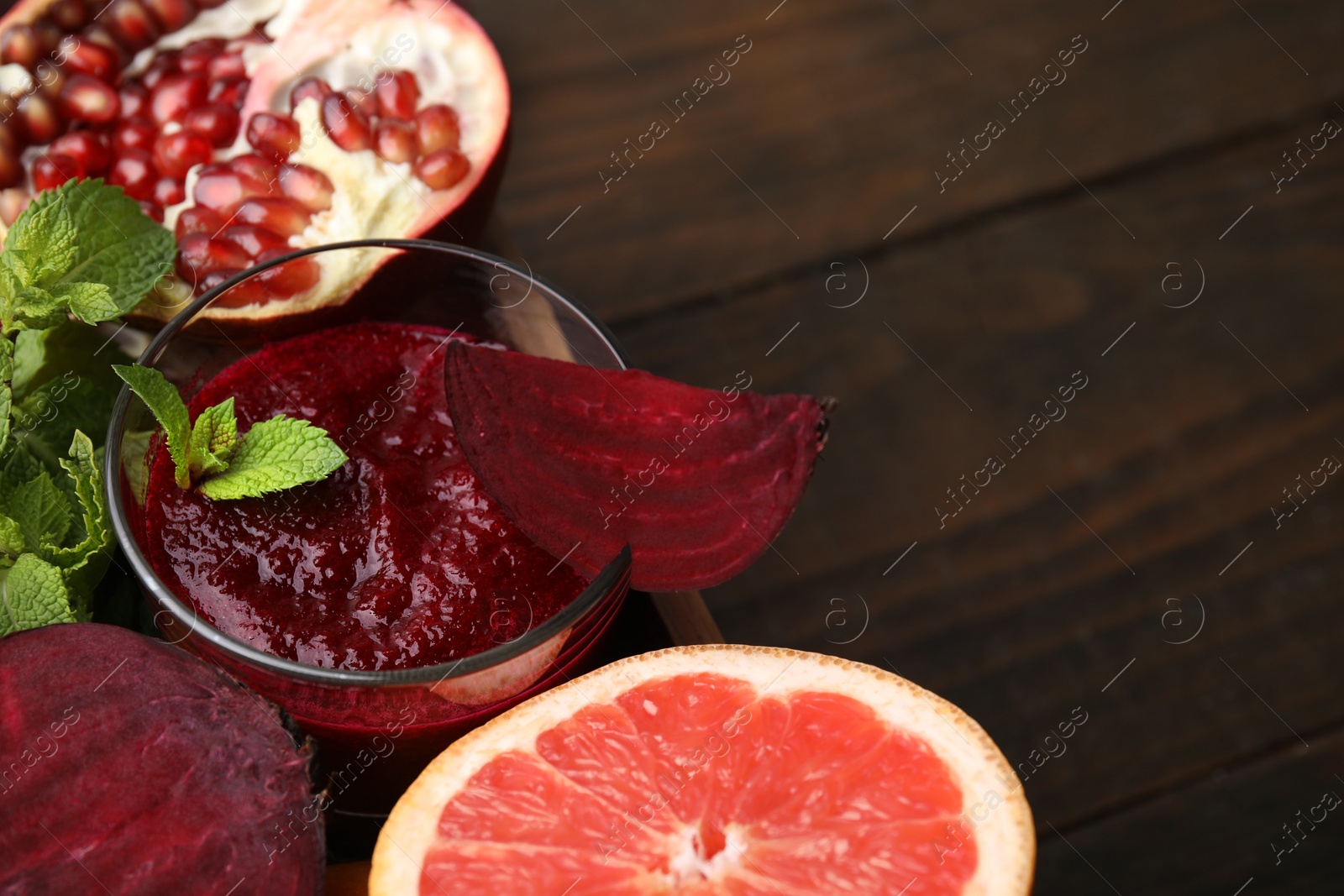 Photo of Vegan drink. Tasty beetroot smoothie in glass, fresh vegetables, fruits and mint on wooden table, closeup. Space for text