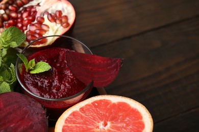 Photo of Vegan drink. Tasty beetroot smoothie in glass, fresh vegetables, fruits and mint on wooden table, closeup. Space for text