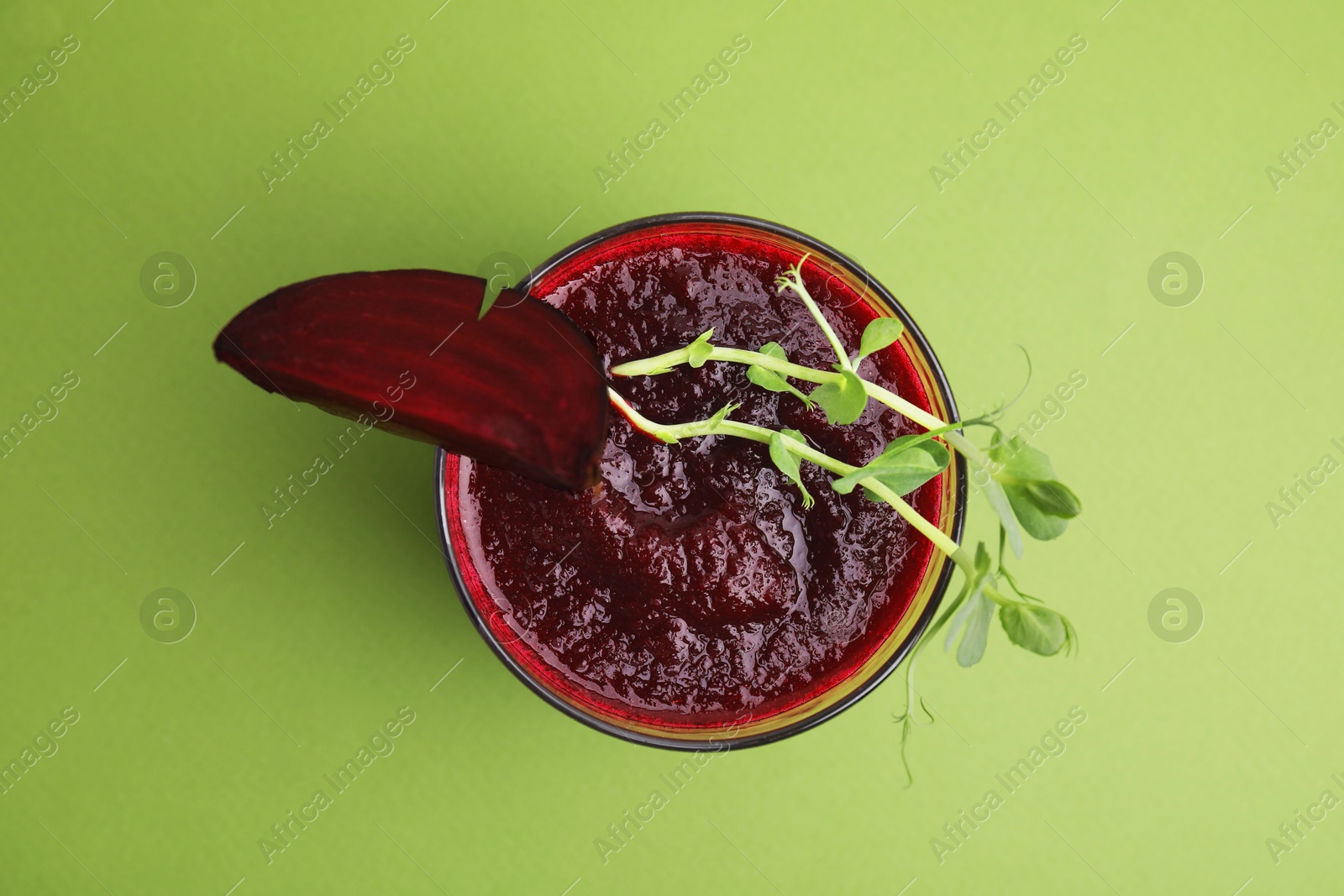 Photo of Tasty beetroot smoothie with microgreens in glass on green table, top view. Vegan drink