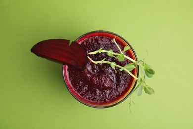 Photo of Tasty beetroot smoothie with microgreens in glass on green table, top view. Vegan drink