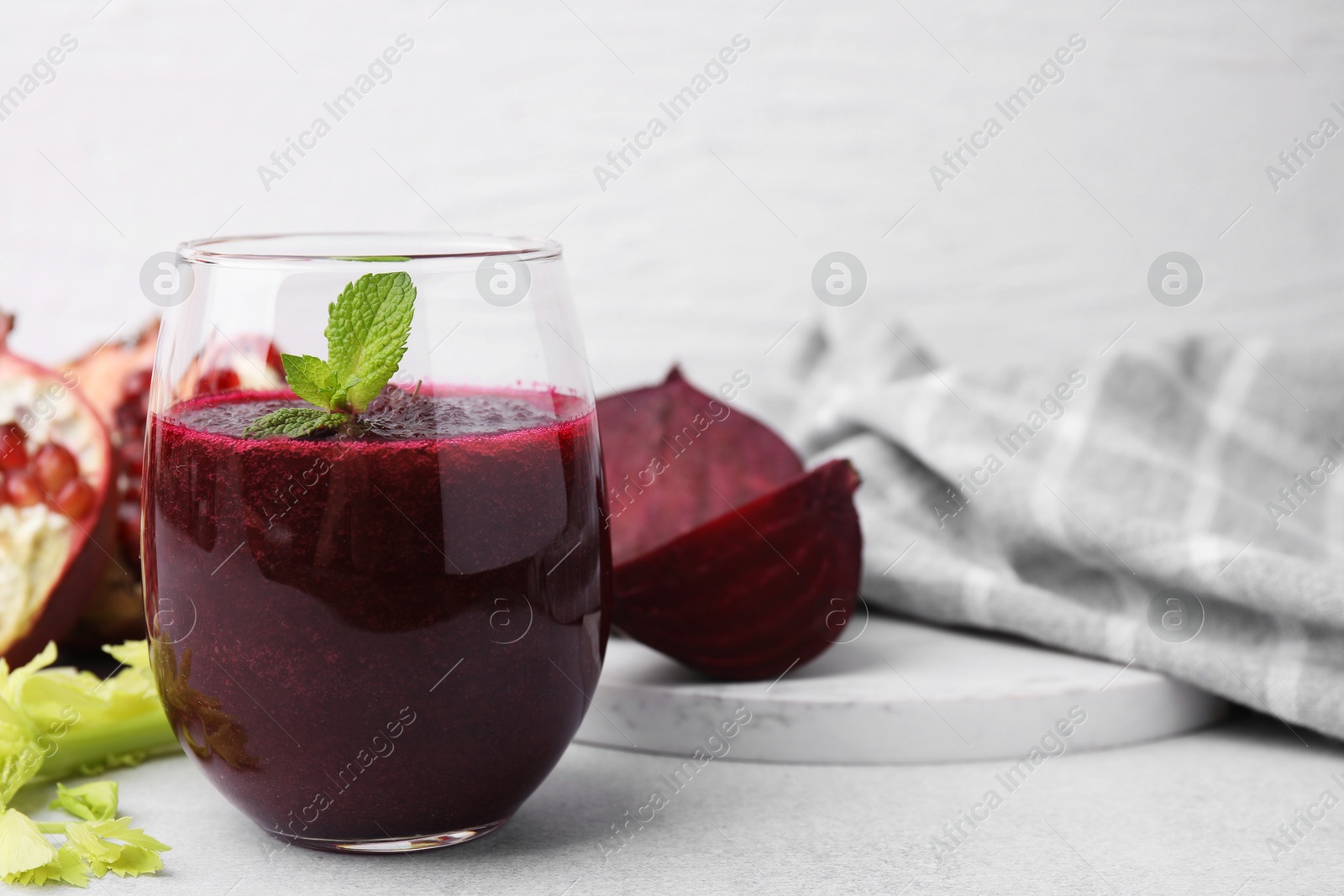 Photo of Tasty beetroot smoothie with mint in glass and fresh vegetables on light table, closeup. Vegan drink