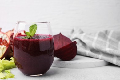 Tasty beetroot smoothie with mint in glass and fresh vegetables on light table, closeup. Vegan drink