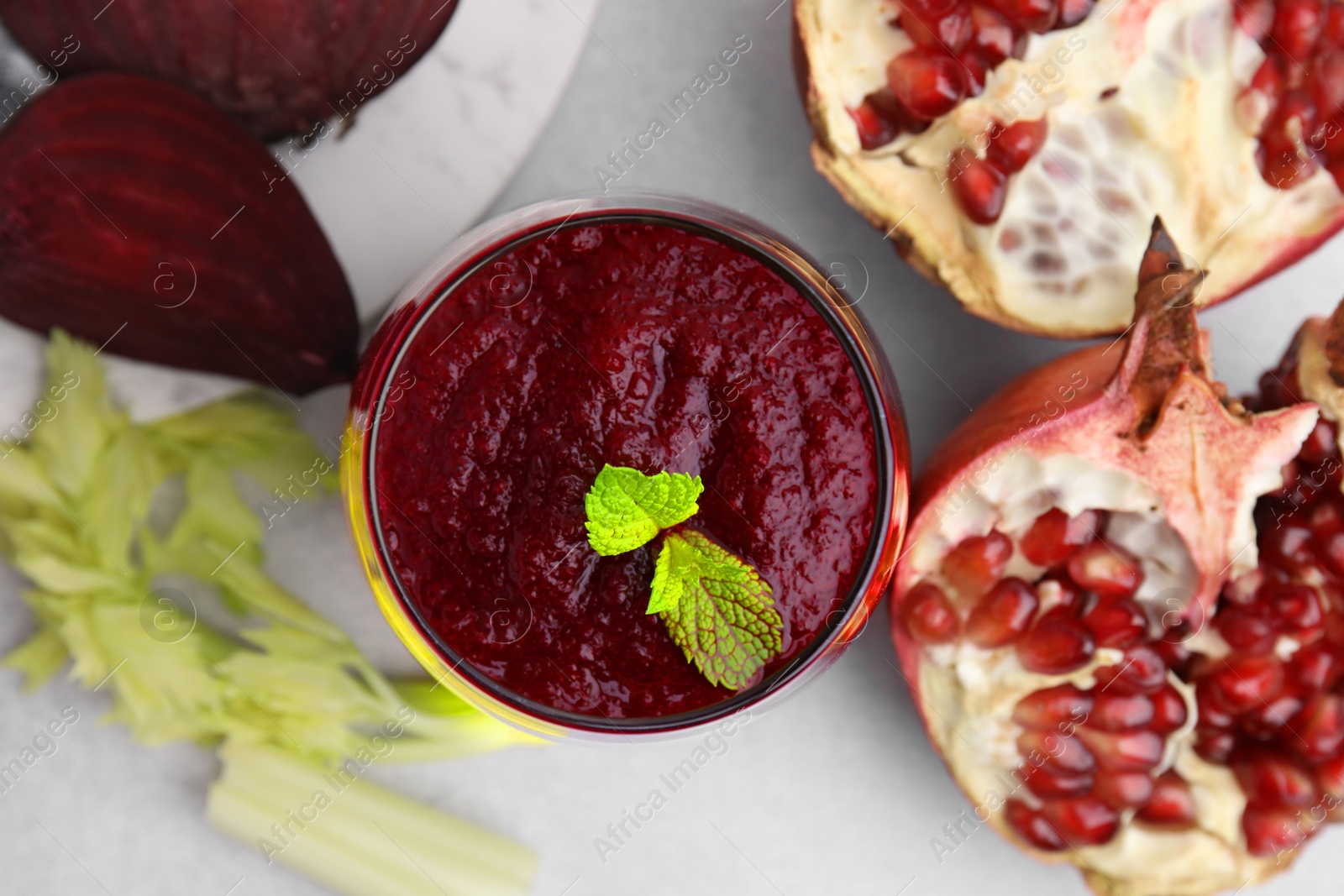 Photo of Tasty beetroot smoothie with mint in glass, fresh vegetables and pomegranate on light table, flat lay. Vegan drink