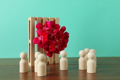 Wooden human figures near beautiful flower on table against turquoise background