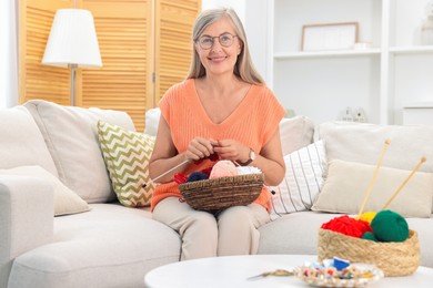 Smiling senior woman knitting on sofa at home