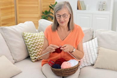 Beautiful senior woman knitting on sofa at home