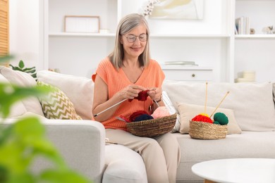 Smiling senior woman knitting on sofa at home