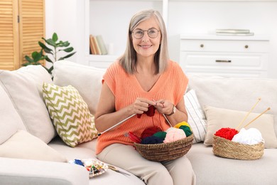 Smiling senior woman knitting on sofa at home