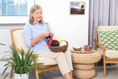 Photo of Beautiful senior woman knitting on armchair at home