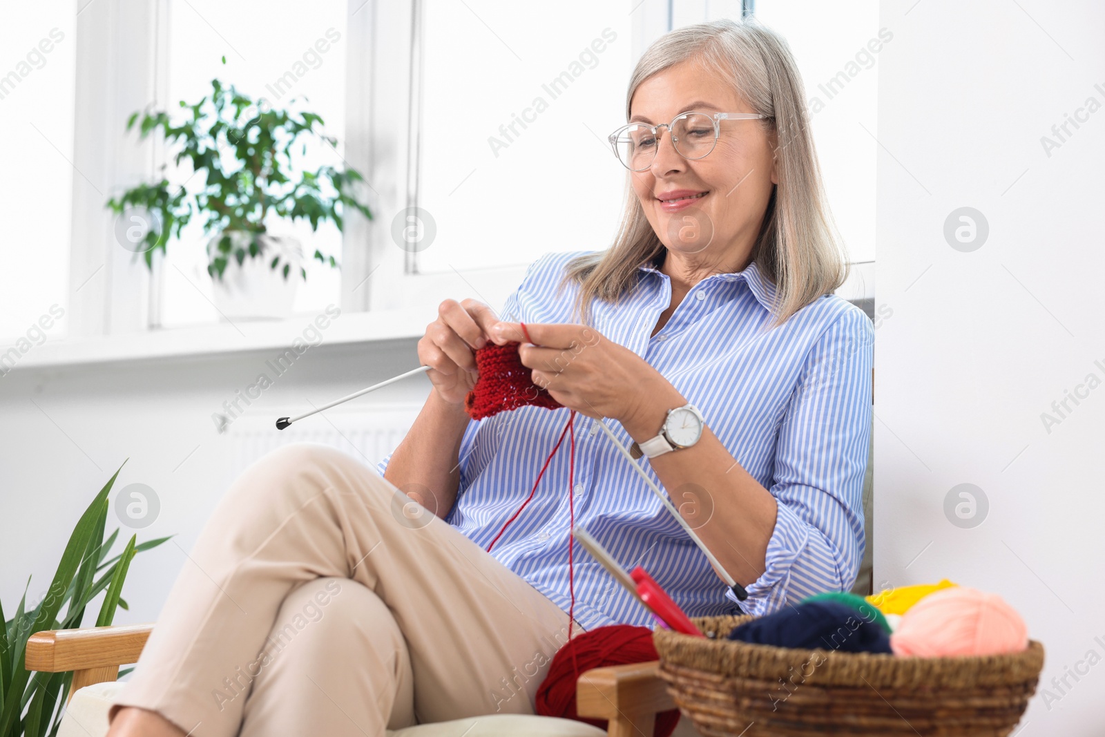 Photo of Smiling senior woman knitting on armchair at home, low angle view