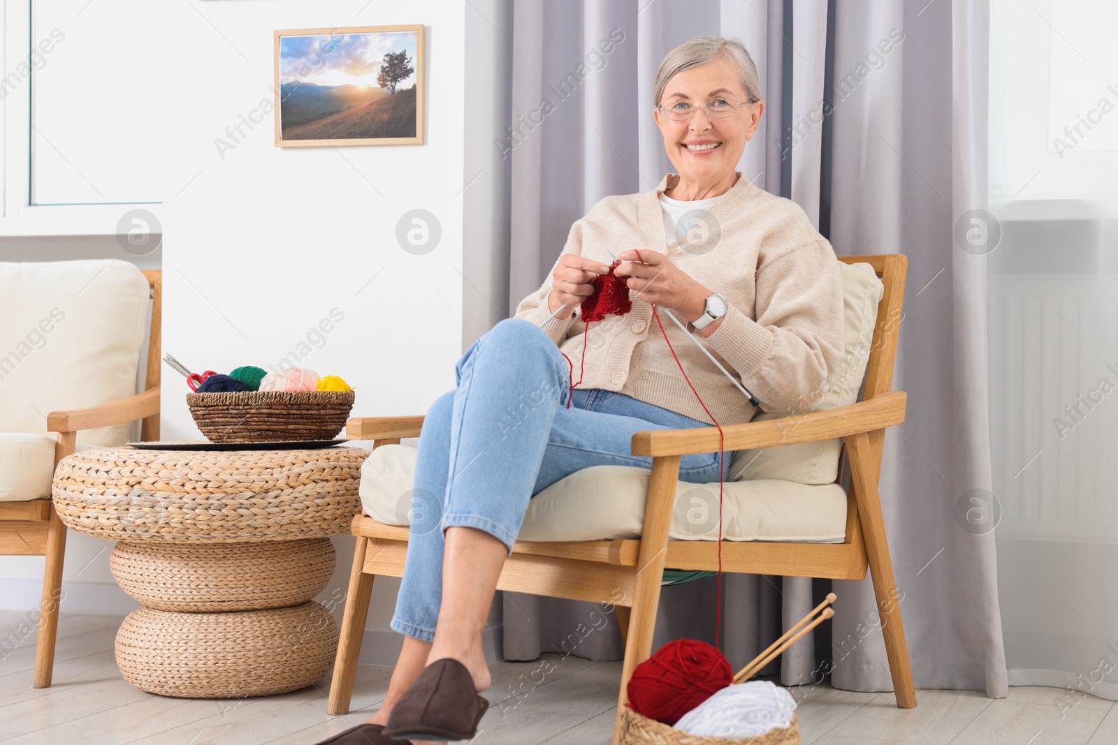 Photo of Smiling senior woman knitting on armchair at home