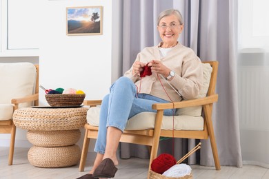 Smiling senior woman knitting on armchair at home