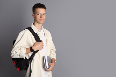 Photo of Portrait of teenage boy with backpack and books on grey background, space for text