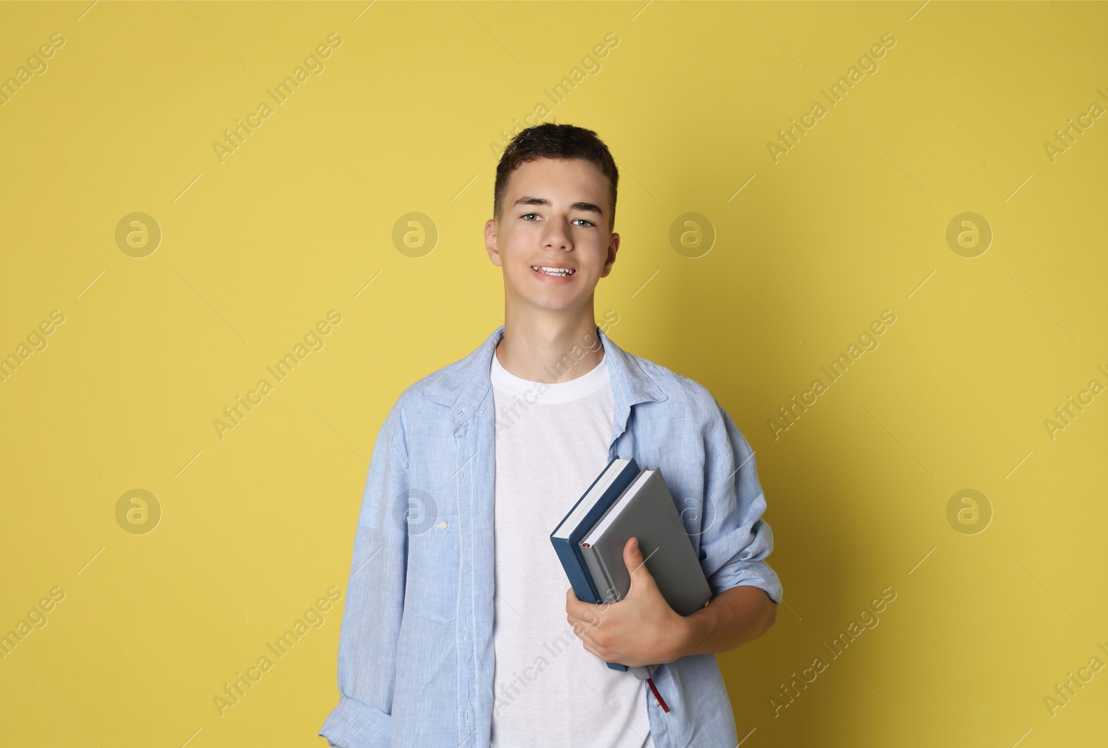 Photo of Portrait of teenage boy with books on yellow background