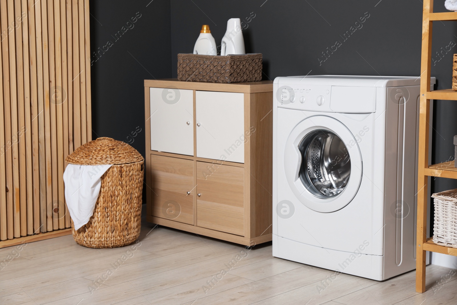 Photo of Washing machine, detergents, laundry basket and storage cabinet indoors