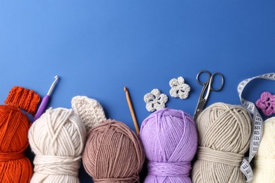 Photo of Different colorful yarns, crochet flowers, hooks and scissors on blue background, flat lay. Space for text