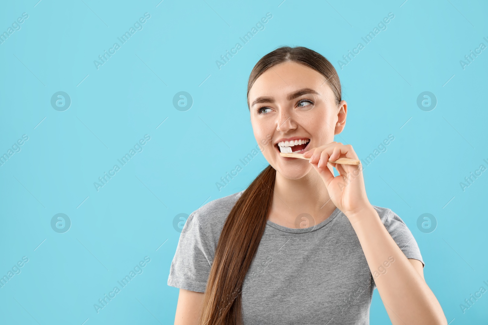 Photo of Beautiful woman brushing her teeth on light blue background, space for text