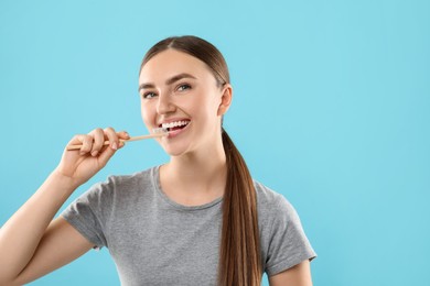 Beautiful woman brushing her teeth on light blue background, space for text