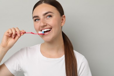 Beautiful woman brushing her teeth on gray background, space for text