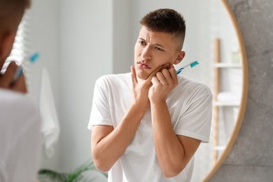 Young man with toothbrush suffering from toothache in bathroom