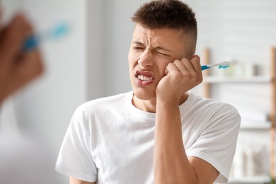 Photo of Young man with toothbrush suffering from toothache in bathroom