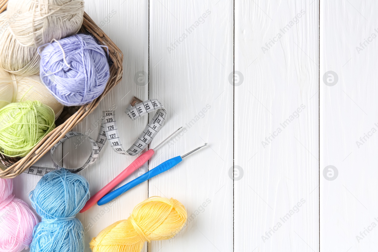 Photo of Crochet hooks, measuring tape and colorful yarns on white wooden table, flat lay. Space for text