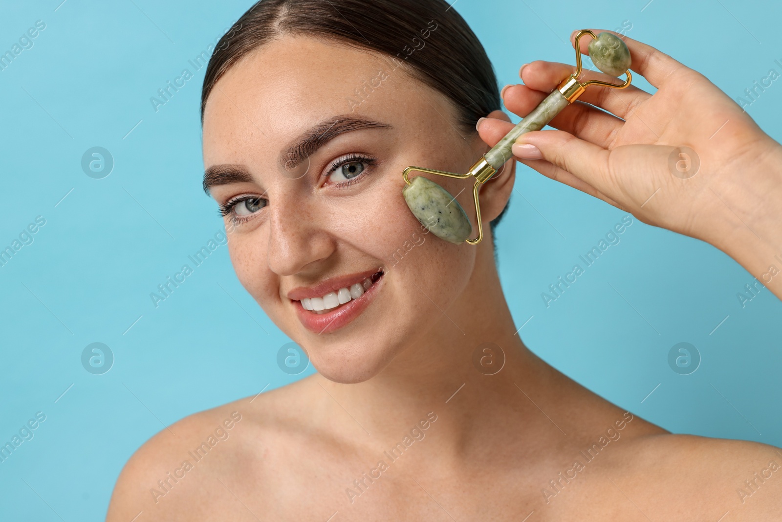 Photo of Beautiful young woman doing facial massage with roller on light blue background