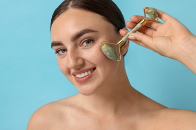 Beautiful young woman doing facial massage with roller on light blue background