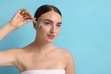 Photo of Beautiful young woman doing facial massage with roller on light blue background, space for text