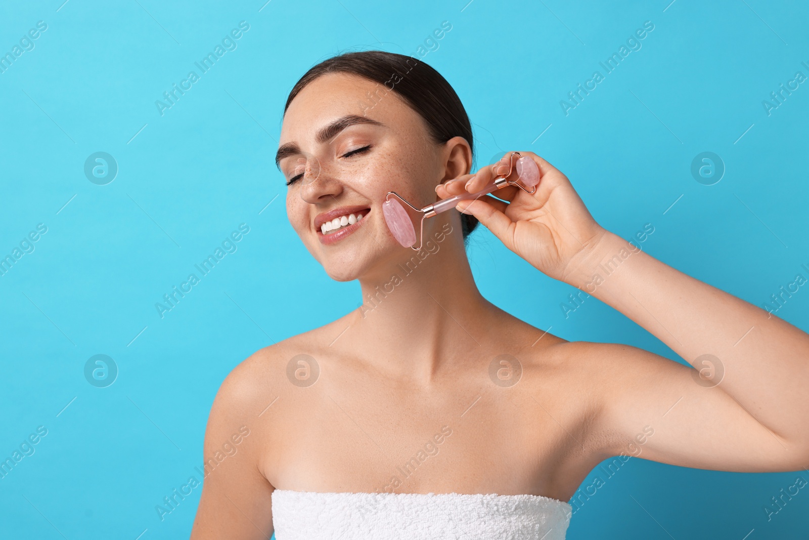 Photo of Beautiful young woman doing facial massage with roller on light blue background