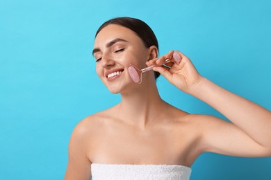 Beautiful young woman doing facial massage with roller on light blue background