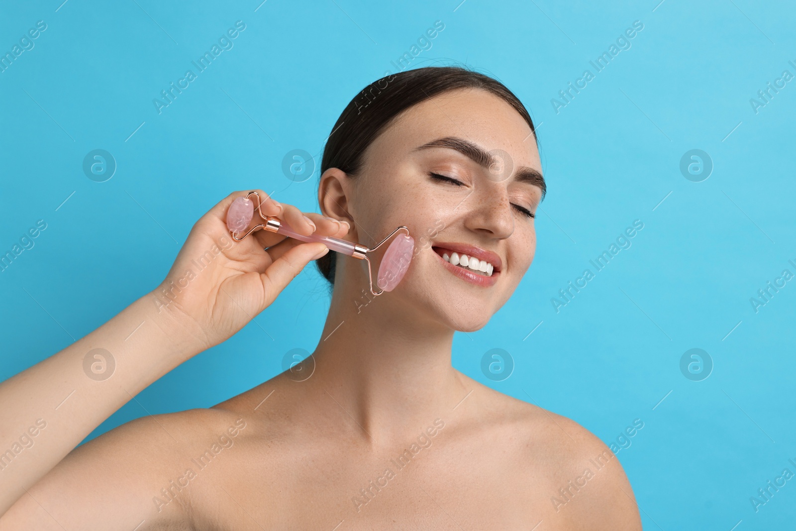 Photo of Beautiful young woman doing facial massage with roller on light blue background