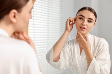 Beautiful young woman doing facial massage near mirror at home