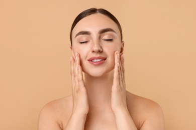 Beautiful young woman doing facial massage on beige background