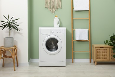 Photo of Washing machine, towels and detergent in laundry room