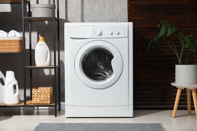 Photo of Washing machine, plant and detergents in laundry room