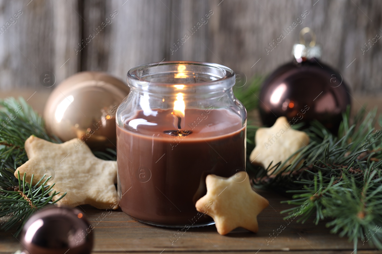 Photo of Burning candle, baubles, cookies and fir branches on wooden table, closeup. Christmas atmosphere