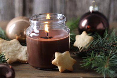 Photo of Burning candle, baubles, cookies and fir branches on wooden table, closeup. Christmas atmosphere