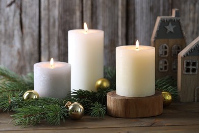 Photo of Burning candles, baubles, fir branches and other Christmas decor on wooden table