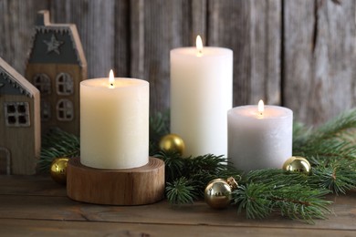 Photo of Burning candles, baubles, fir branches and other Christmas decor on wooden table