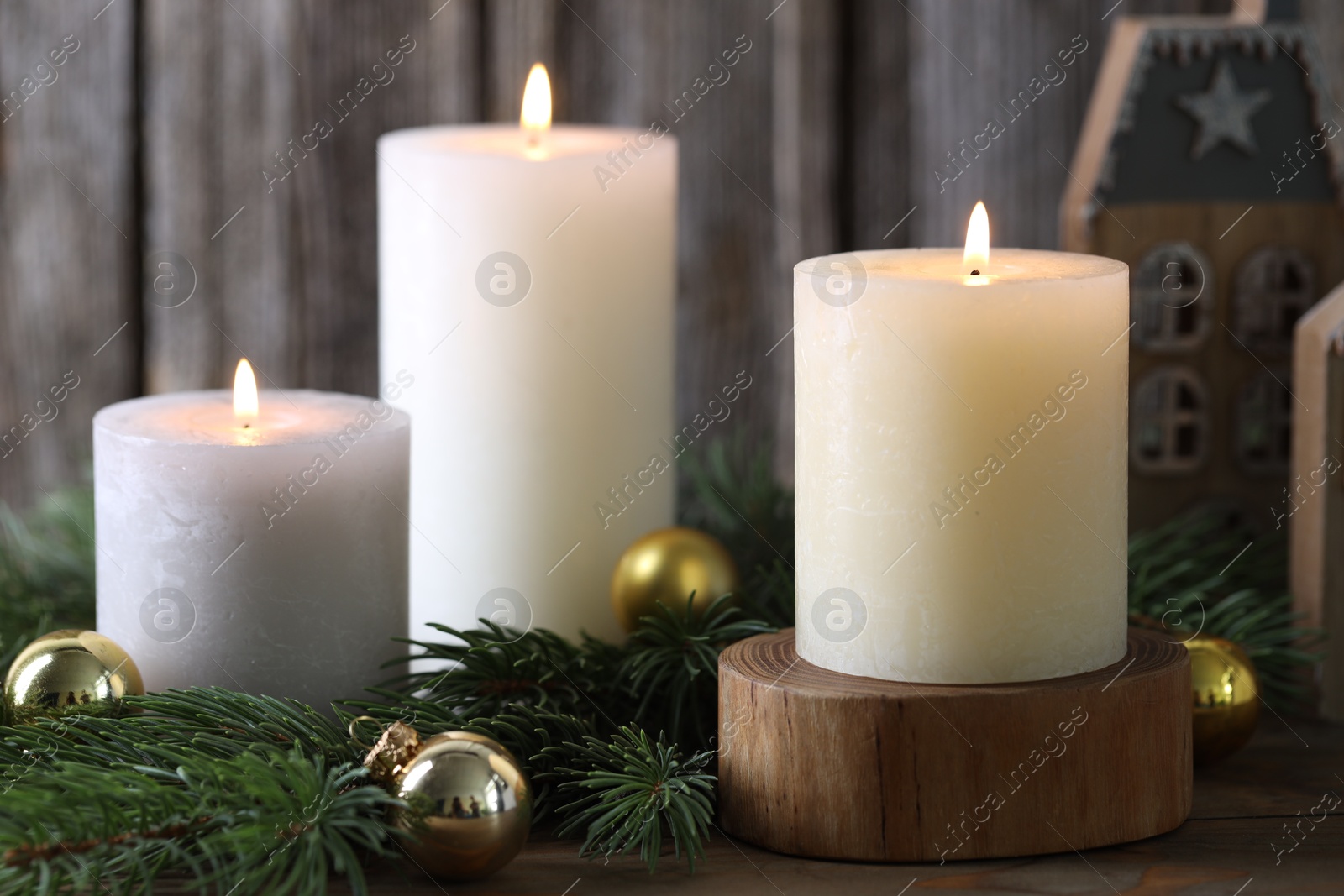 Photo of Burning candles, baubles and fir branches on wooden table, closeup. Christmas atmosphere