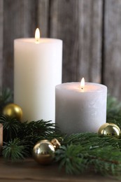 Photo of Burning candles, baubles and fir branches on wooden table, closeup. Christmas atmosphere