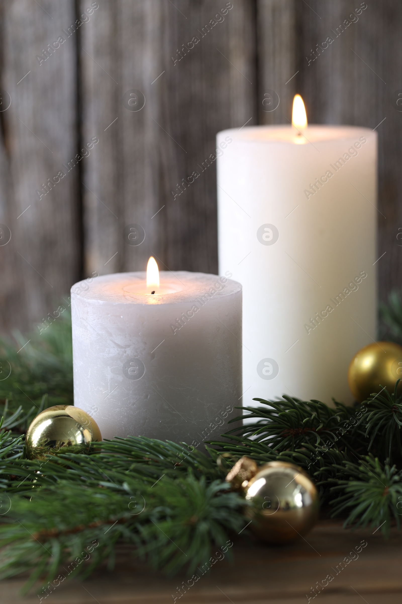 Photo of Burning candles, baubles and fir branches on wooden table, closeup. Christmas atmosphere