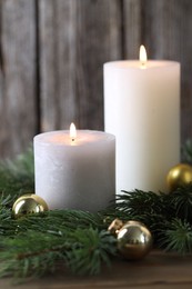 Photo of Burning candles, baubles and fir branches on wooden table, closeup. Christmas atmosphere